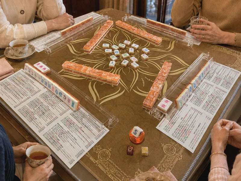 Four participants around a mah jongg table, with hands, cups and tile racks visible at all four places