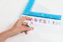 Azure Tropics American Mah Jongg flower tile held in a hand beside an aqua tile wall