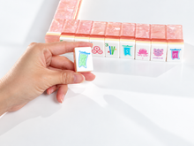 Blush Lotus American Mah Jongg direction tile held in a hand beside a pink tile wall