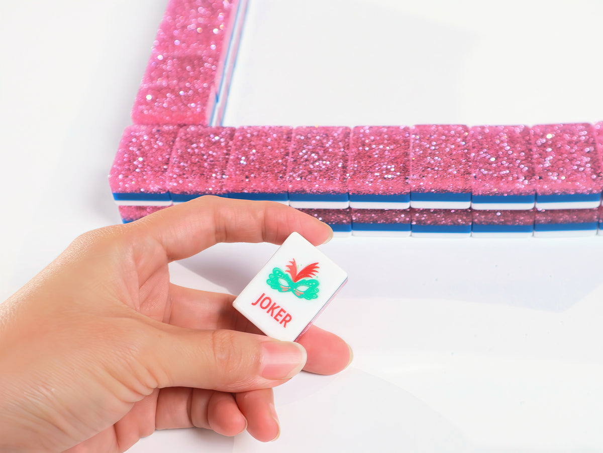 Pink Stardust American Mah Jongg Joker tile held in a hand beside a pink tile wall