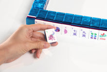 Sapphire Pavilion American Mah Jongg illustrated tile held in a hand beside a blue tile wall