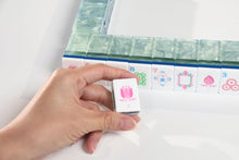 Sea Glass Lotus American Mah Jongg lotus tile held in a hand beside a green tile wall