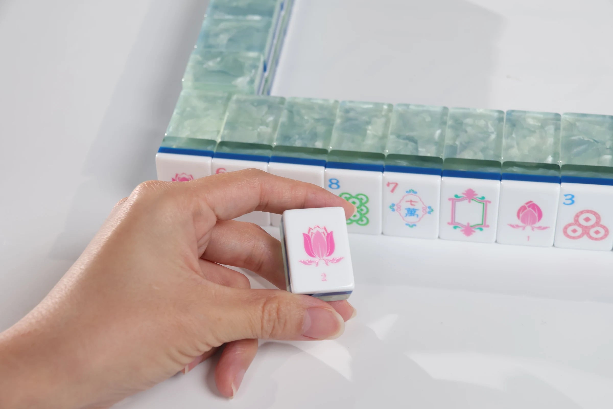 A hand holding a Sea Glass Lotus American Mah Jongg tile beside coordinated racks and tiles